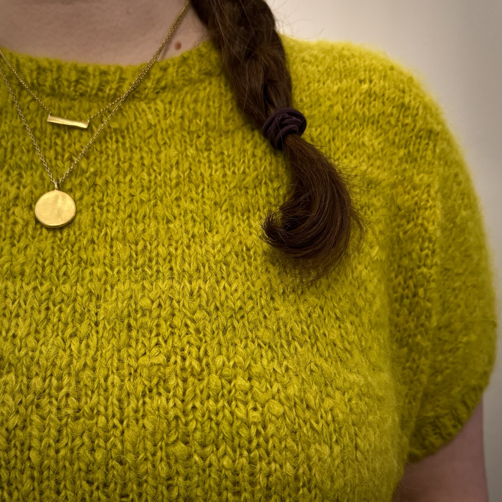 A close-up shot of a fluffy, hand-knit sweater. The sweater is chartreuse in color and has short sleeves. It appears soft to the touch.